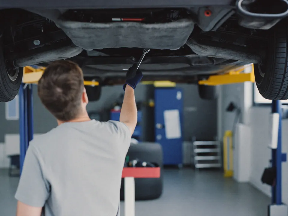 A mechanic works under a car raised on a lift in a clean service bay.