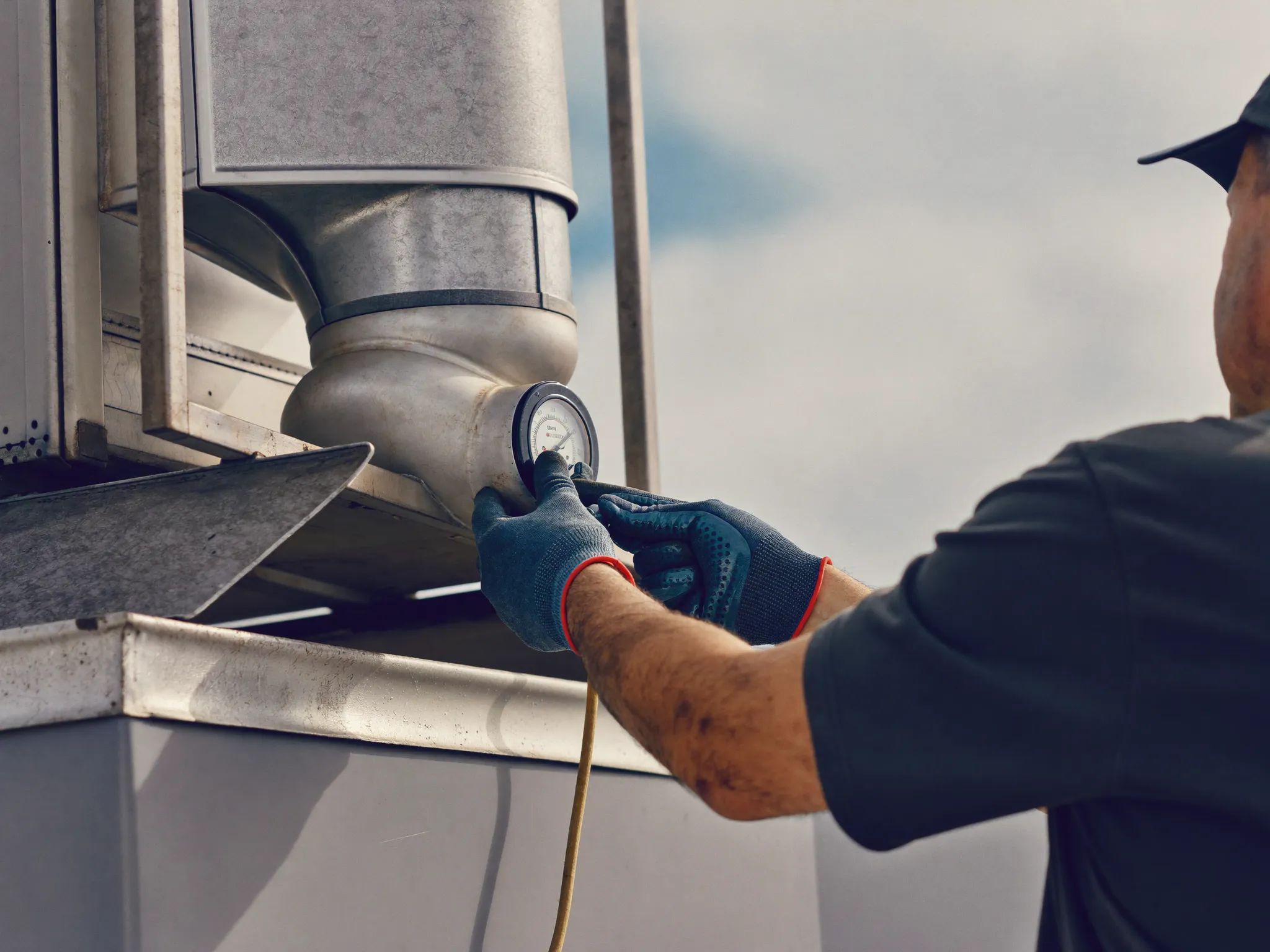 A technician checking a pressure gauge on a rooftop HVAC unit