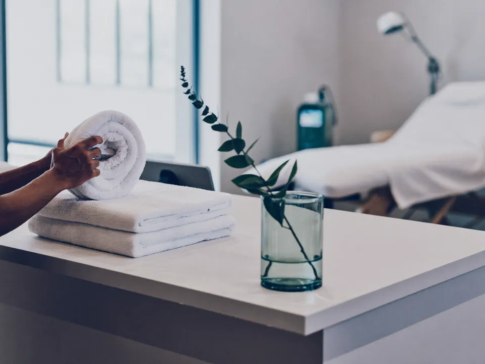 Freshly rolled towels being set out on a med spa front desk, with a treatment room in the background.