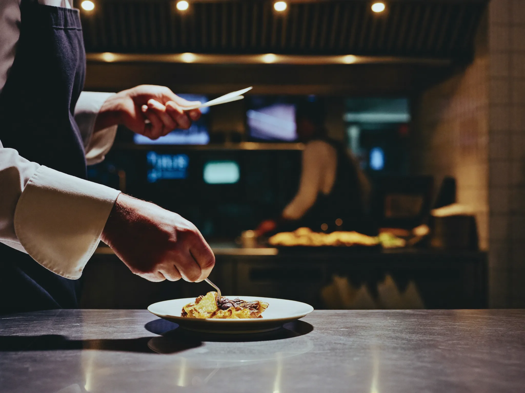 A chef plating a dish at the kitchen pass during service